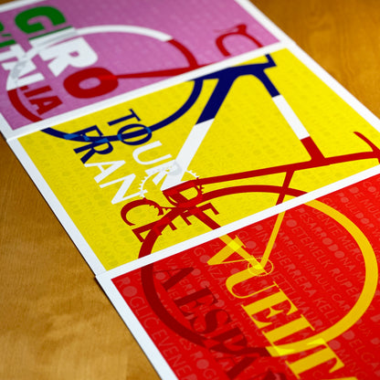 Close-up of Grand Tour cycling event posters on a wooden surface