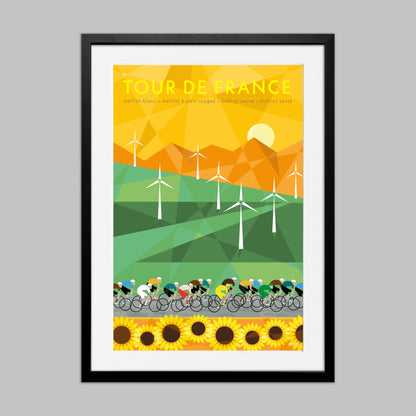 Cycling print of the Tour de France peloton racing past a field of windmills and sunflowers with mountains in the background. The yellow jersey can be seen in the group. Presented in a black frame with a white mount